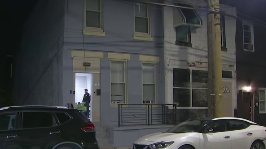 A police officer is illuminated in the doorway of a home along North 32nd Street in Philly's Strawberry Mansion section where a man was killed in a shooting on Monday night.