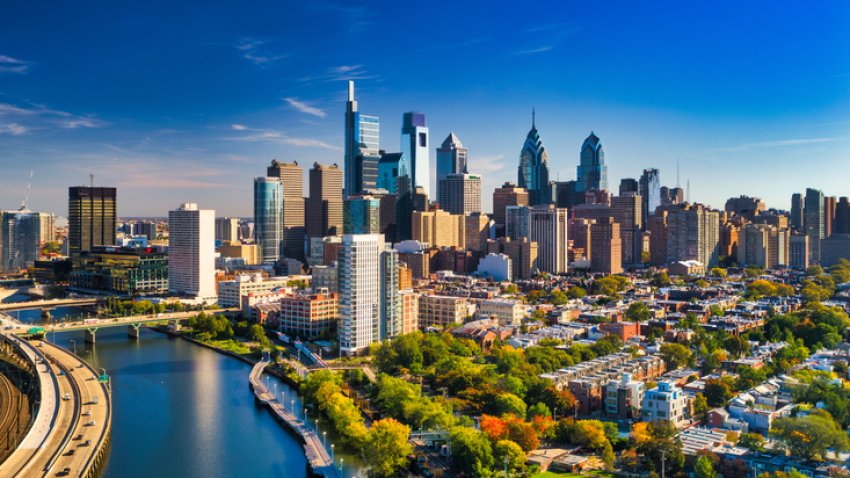 Philadelphia skyline aerial view with the Schuylkill River, Schuylkill Expressway and residential neighborhoods and autumn colored trees in the foreground, and a blue sky with clouds in the background.