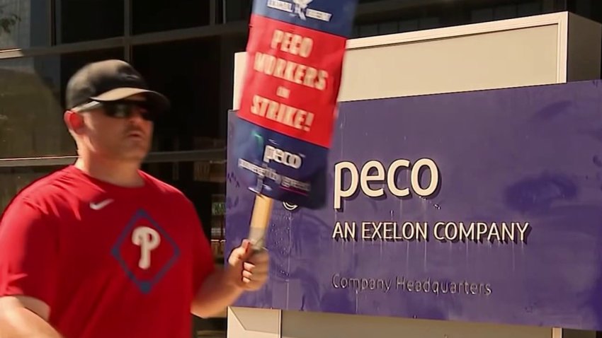 A worker on strike walks in front of a sign at PECO's headquarters in Philly during a recent strike.