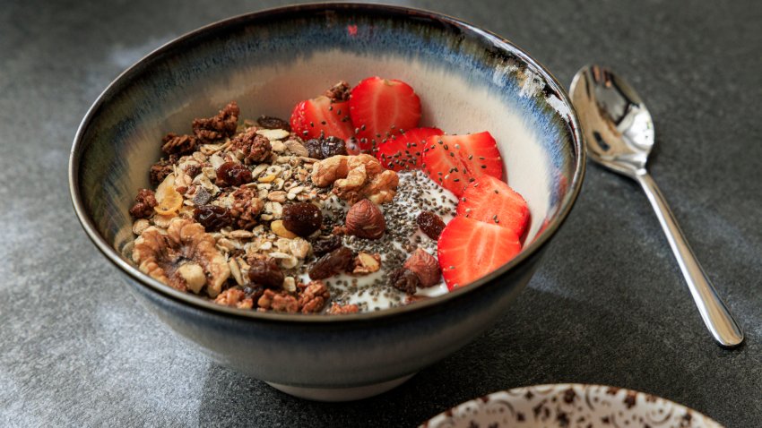 Bowl with yogurt topped with crunchy granola, fresh sliced strawberries, walnuts, hazelnuts, raisins, and chia seeds.